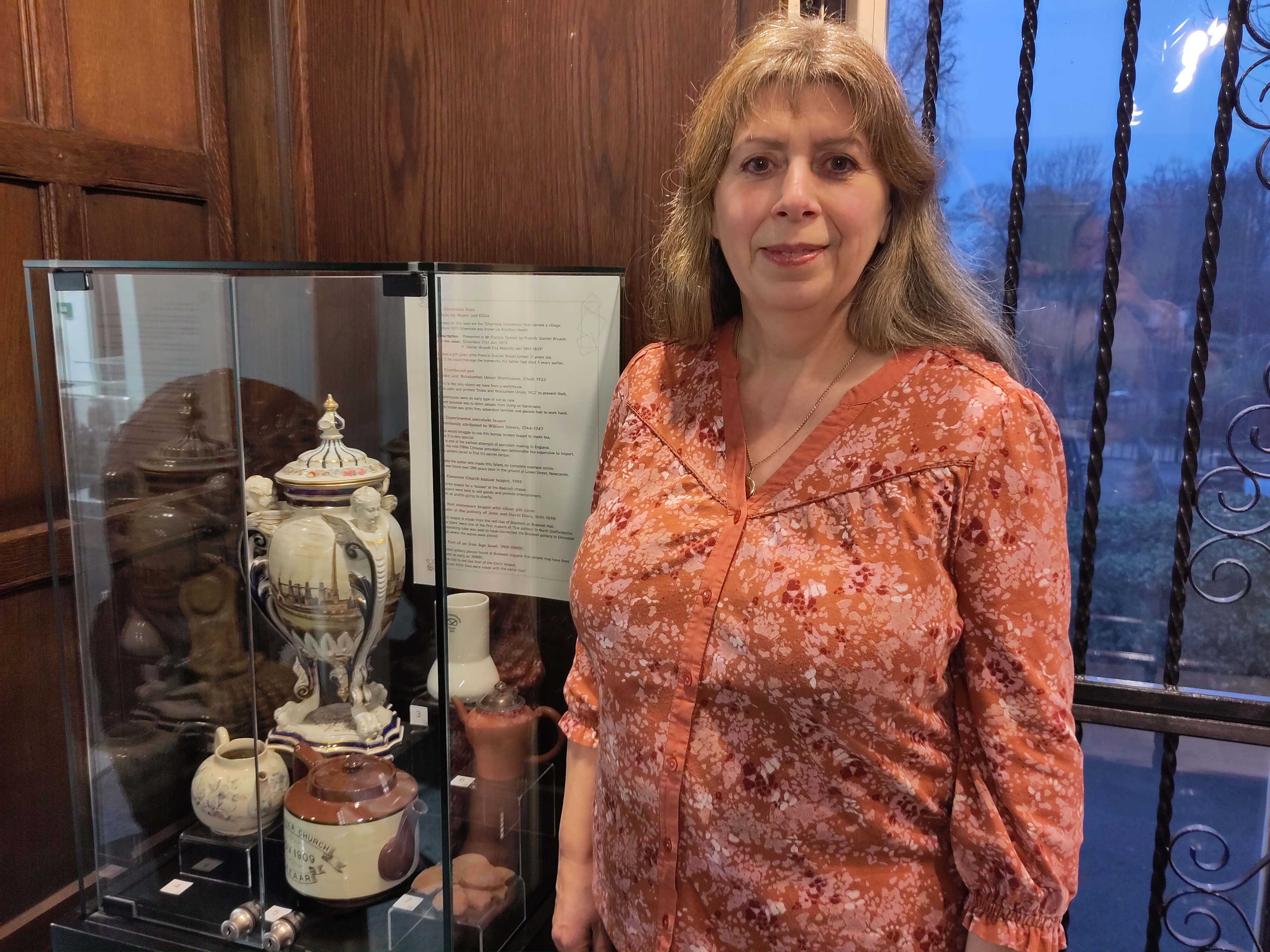 A woman stands next to a museum case filled with ceramics