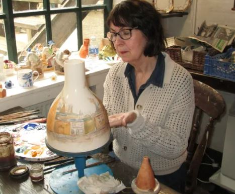 A woman paints onto a large ceramic pot